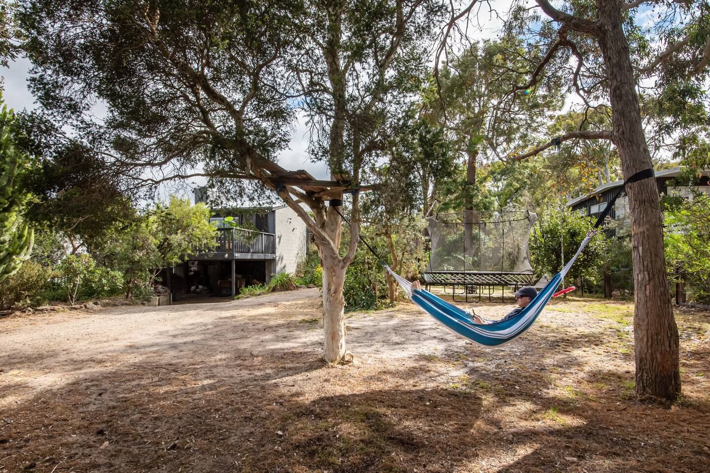 A hammock strung between trees in the backyard, with the trampoline behind