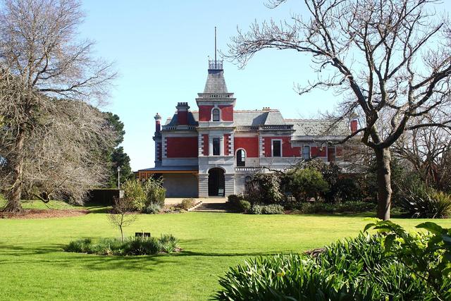 Red brick Coolart Homestead with its tower behind bare winter trees and a lawn near Somers, Victoria