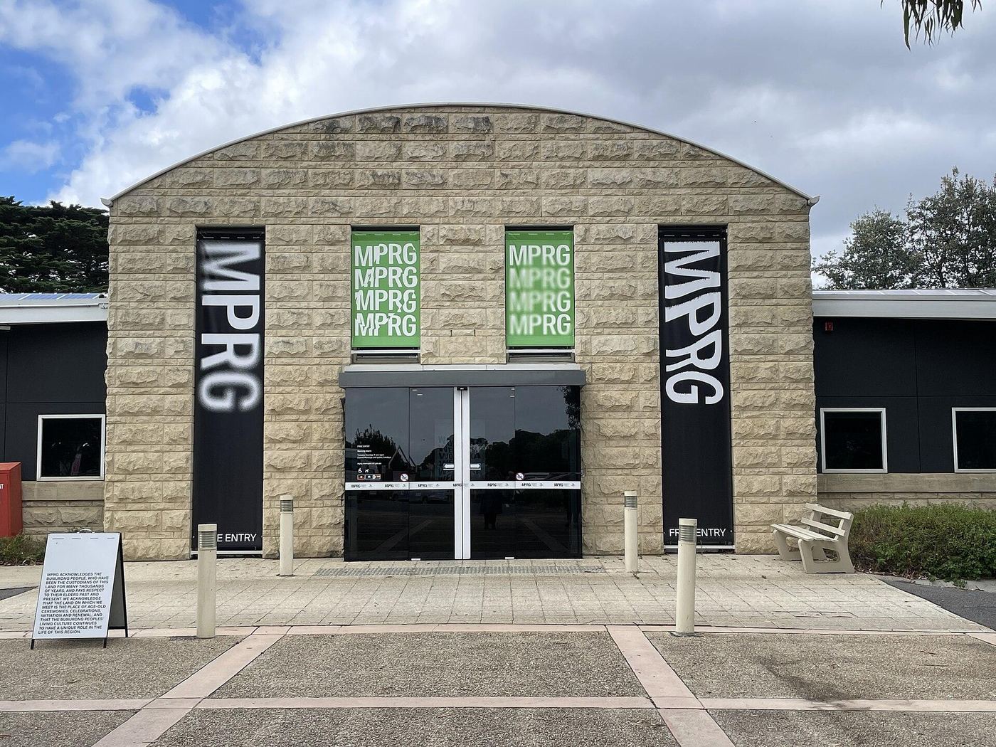 Stone-clad entrance of the Mornington Peninsula Regional Gallery with its vaulted roof, gallery banners hung either side of the doors